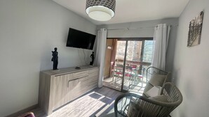 Una sala de estar moderna con un televisor de pantalla plana, un mueble de madera, una mesa de vidrio y una silla de mimbre.