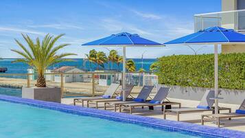 Uma área de piscina com espreguiçadeiras e guarda-sóis, com vista para uma praia e o oceano.