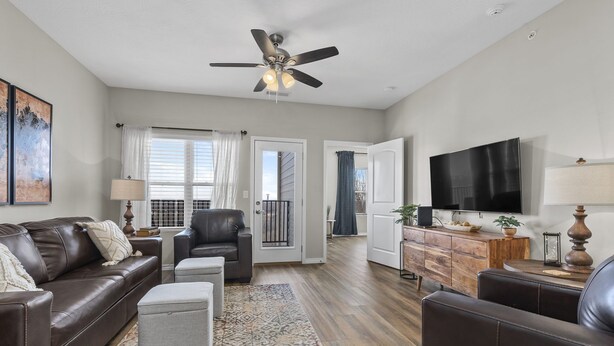 A modern living room with a brown leather sofa, a grey ottoman, a wooden coffee table, and a TV on a wooden cabinet. - Matt's Adventure Condo (Branson)