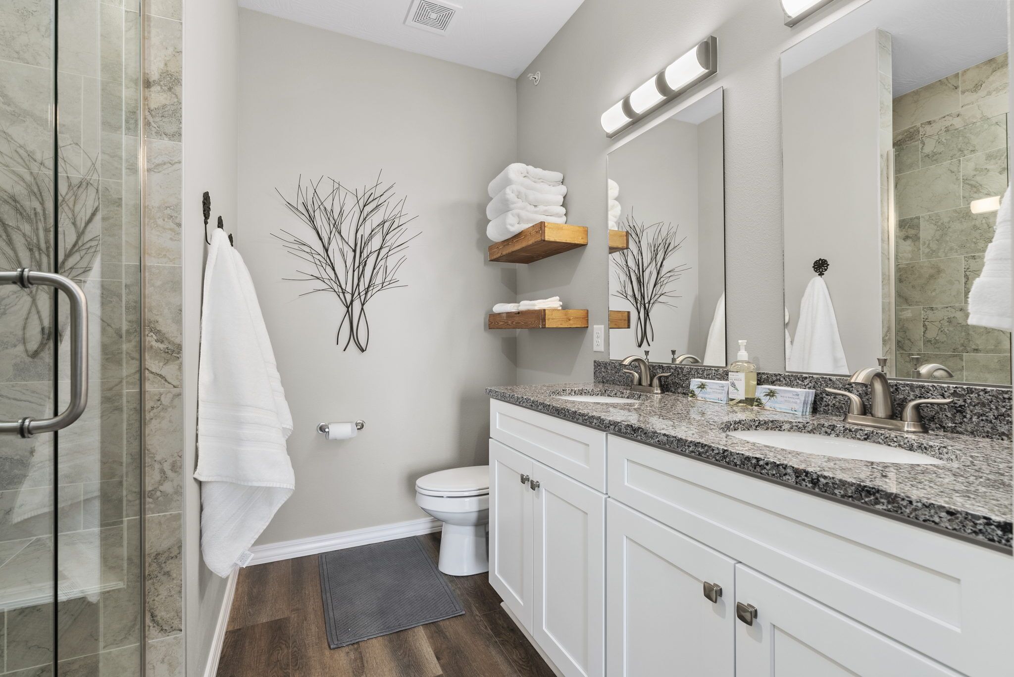 A modern bathroom with a glass shower enclosure, white cabinets, a granite countertop, and a large mirror.