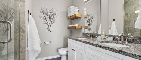 A modern bathroom with a glass shower enclosure, white cabinets, a granite countertop, and a large mirror.