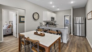 A modern kitchen with white cabinets, a stainless steel refrigerator, and a dining area with a marble table and wooden chairs. - Matt's Adventure Condo (Branson)