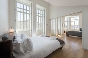 Une chambre moderne avec un grand lit, une table de chevet et un canapé, le tout dans une pièce lumineuse dotée de grandes fenêtres.