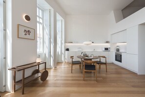 Une cuisine moderne avec des meubles blancs, un coin repas doté d’une table ronde et de chaises, ainsi qu’un banc en bois avec une lampe.