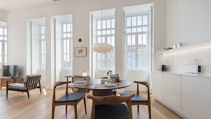 A modern kitchen with white cabinets, a dining area with wooden chairs, and large windows providing natural light.