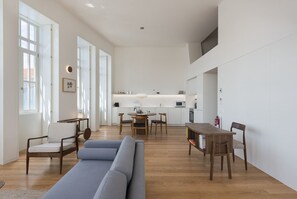 Un grand espace de vie comprenant un canapé, des fauteuils, une table à manger et une cuisine à l’arrière-plan.