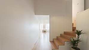 A modern interior with a wooden staircase, a potted plant, and a hallway leading to a dining area.