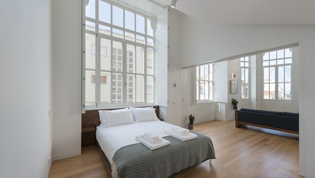 Un dormitorio amplio con una cama grande, un banco y vistas de la ciudad a través de amplias ventanas.