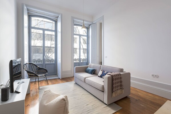 A modern living room with a sofa, a chair, a desk, and a large window.