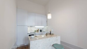 Cozinha moderna com armários brancos, bancada de mármore e dois banquetas.