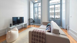 Uma sala de estar moderna com uma TV de tela plana, um sofá, um pufe e uma poltrona.