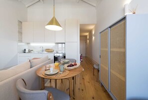 A modern kitchen with white cabinets, a wooden dining table set with plates, cups, and a fruit basket.