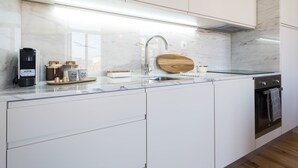 Eine moderne Küche mit weißen Schränken, einer Marmorarbeitsplatte, einem eingebauten Backofen und einer Kaffeemaschine.