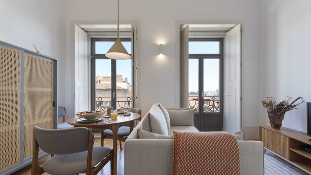 Ein modernes Wohnzimmer mit einer Couch, Sesseln, einem Esstisch und Blick auf die Stadt durch große Fenster.