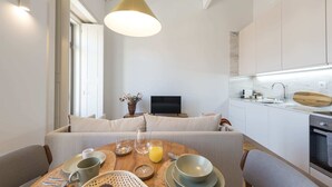 Eine moderne Küche mit weißen Schränken, ein Essbereich mit rundem Tisch und eine Sitzecke mit Sofa.