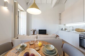 A modern kitchen with white cabinets, a dining area with a round table, and a sofa.