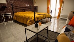 A hotel room with a bed, a small table with a vase, a chair, and a sofa. - Agora Holiday House (Palazzolo Acreide)