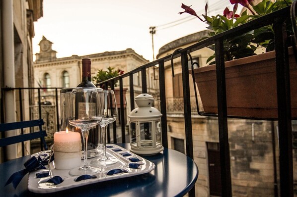 A table with a candle, wine glasses, and a lantern on a balcony with a view of a historic building.