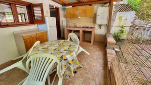 A compact kitchen with wooden cabinets, a gas stove, and a refrigerator. There is a dining table with chairs and a hanging light fixture. - Blue Med Scooby, Palinuro, Cilento (Palinuro)