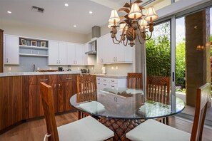Cozinha moderna com armários de madeira, mesa de jantar de vidro e um lustre diferenciado.