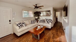 A living room with a white sectional sofa, a wooden coffee table, a ceiling fan, and a large mirror. - The Apartment Suite! Private Hot Tub w/ Mountain Views (Colorado Springs)