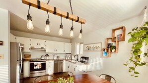 A modern kitchen with white cabinets, a wooden dining table with potted plants, and a hanging light fixture. - The Apartment Suite! Private Hot Tub w/ Mountain Views (Colorado Springs)