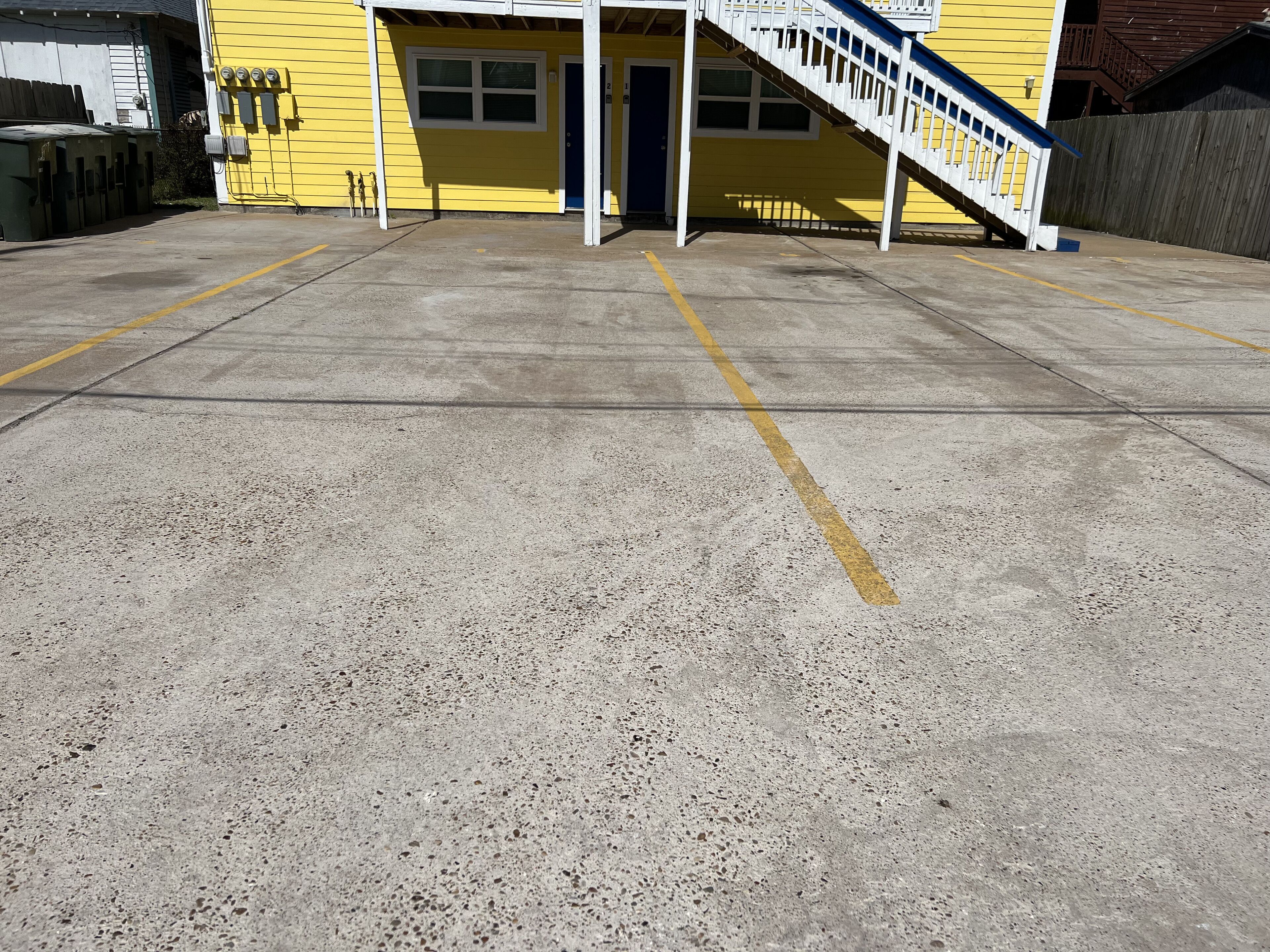 Un bâtiment à la façade jaune, avec une porte bleue et un escalier blanc menant à une zone abritée.