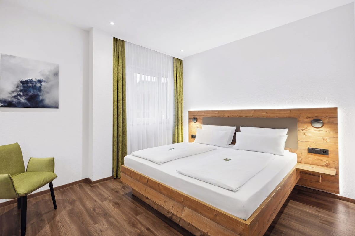Ein modernes Hotelzimmer mit einem Bettgestell aus Holz, einem grünen Sessel und einem Bild an der Wand.