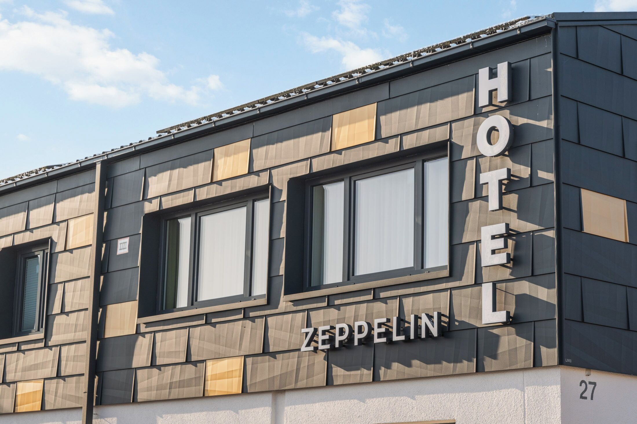 Un hotel llamado 'Zeppelin' con fachada moderna, ventanas amplias y el número de habitación '27' visible.