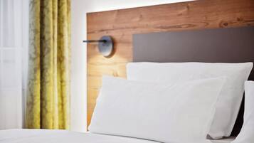 A modern hotel room with a wooden headboard, white bedding, and a wall-mounted lamp.