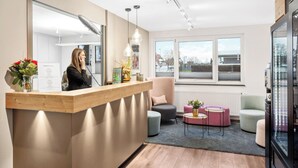 Una recepción moderna con mostrador de madera, asientos con cojines y un amplio ventanal con vistas al exterior.