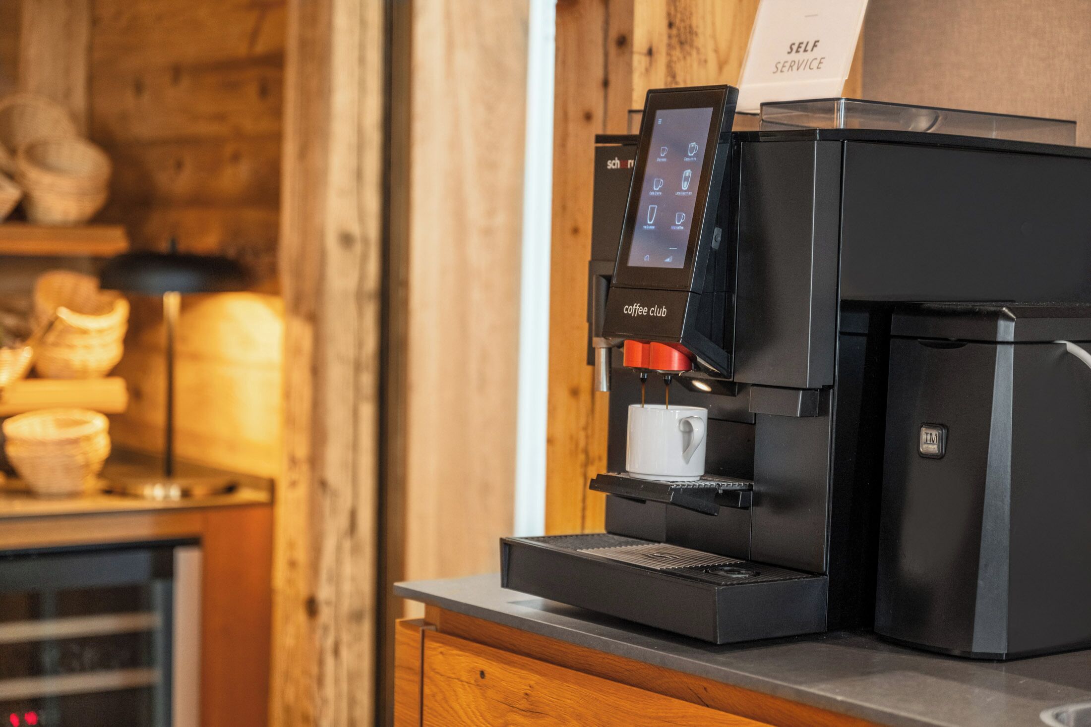 A coffee machine with a touchscreen interface and a self-service sign.