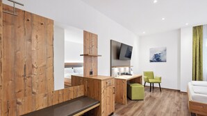 Una habitación de hotel moderna con un armario de madera, un escritorio con televisor de pantalla plana, una silla verde, un reposapiés verde y una cama con ropa de cama blanca.