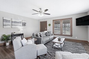 A modern living room with a grey sofa, a coffee table, a TV, and a ceiling fan.