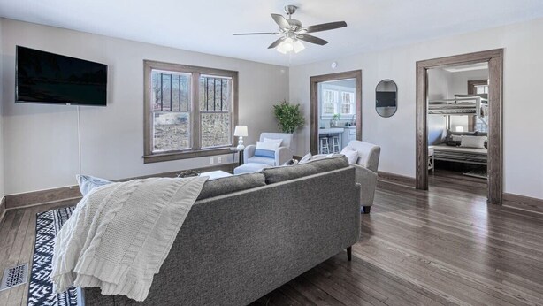 A modern bedroom with a gray sofa, a ceiling fan, a TV, and a large window. - Red Bud (Chattanooga)