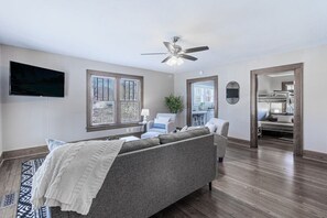 A modern bedroom with a gray sofa, a ceiling fan, a TV, and a large window. - Red Bud (Chattanooga)