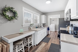 A modern kitchen with white cabinetry, a bar area with stools, a built-in oven, and a refrigerator.