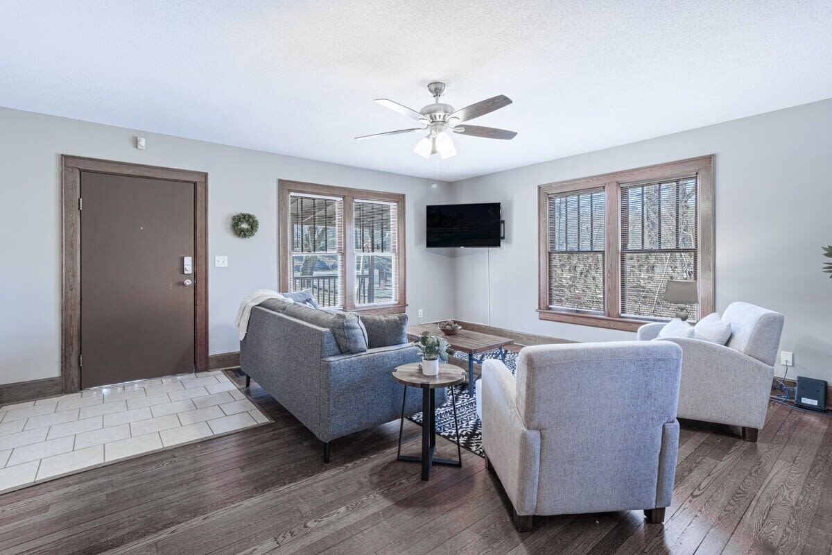 A living room with two sofas, a coffee table, a ceiling fan, and a TV mounted on the wall.