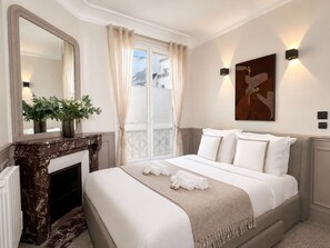 A hotel room with a bed, a fireplace, a large mirror, a window with curtains, and a painting on the wall. - Charming flat with lift - Eiffel Tower (Paris)