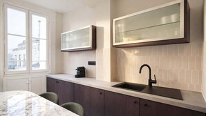 A modern kitchen with a marble countertop, dark cabinets, a black sink, and a window with a city view. - Charming flat with lift - Eiffel Tower (Paris)