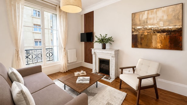 A living room with a sofa, armchair, coffee table, fireplace, and a painting on the wall.