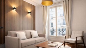 A modern living room with a sofa, a coffee table, and a chair. There is a window with curtains and a view of buildings outside. - Charming flat with lift - Eiffel Tower (Paris)