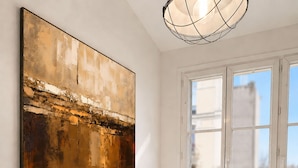 A dining area with a marble table, green upholstered chairs, a large abstract painting, and a window with a view.