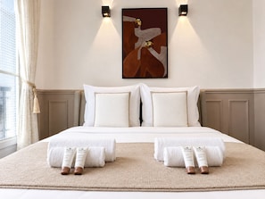 Une chambre d’hôtel avec un grand lit, deux lampes fixées au mur, un tableau et une fenêtre avec des rideaux.