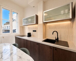 A modern kitchen with a built-in stove, a sink, and a window overlooking a building. - Charming flat with lift - Eiffel Tower (Paris)