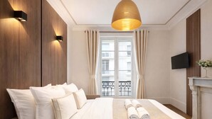 A hotel room with a large bed, a television, a fireplace, and a balcony with curtains. - Charming flat with lift - Eiffel Tower (Paris)