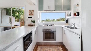 Una cocina moderna con armarios blancos, horno integrado y ventana con vista a la vegetación.