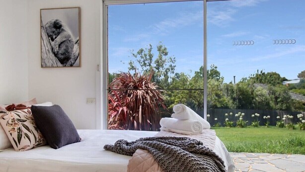 Un dormitorio con un ventanal grande, una cama con colcha, almohadas y un cuadro enmarcado en la pared.