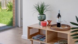 Una sala moderna con una mesa consola de madera, un espejo redondo, una planta en maceta, una botella de vino y copas.