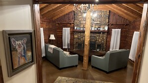 A cozy attic room with a fireplace, two grey sofas, a chandelier, and a framed picture on the wall.